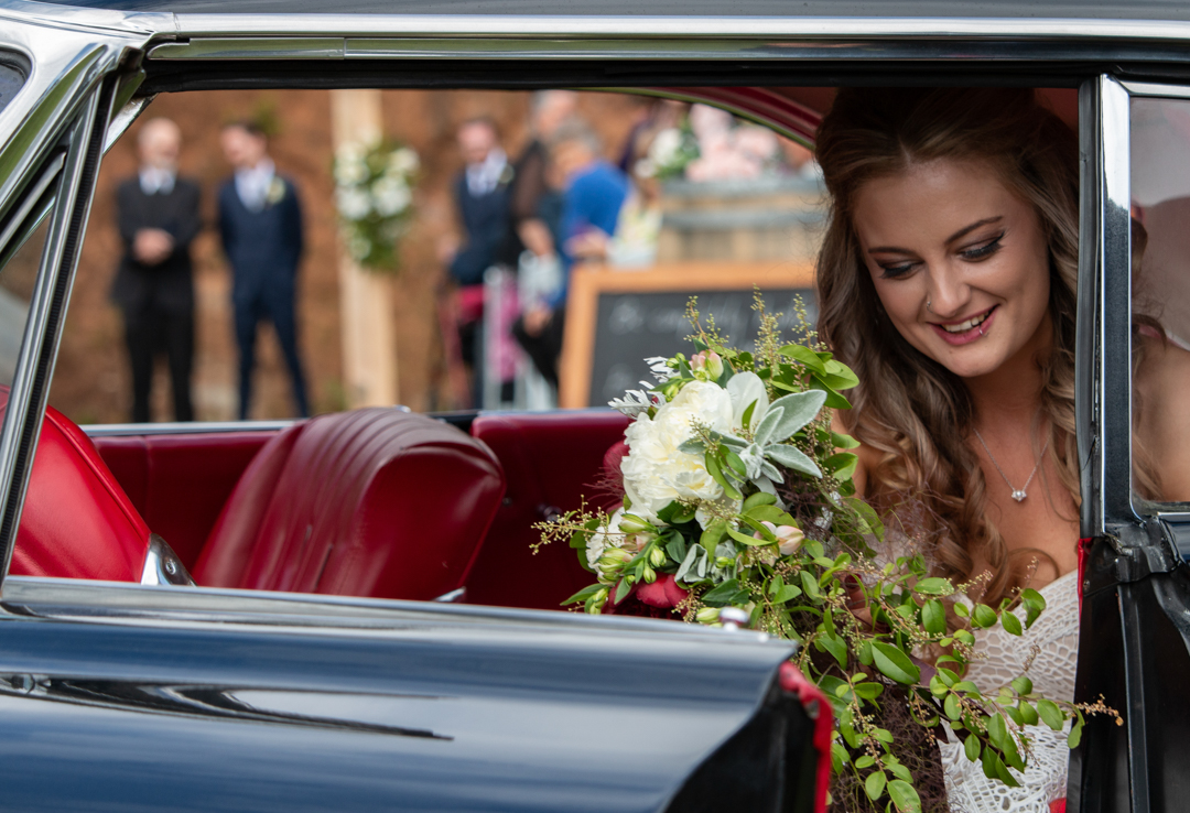 Bride getting out of her car with groom in the background